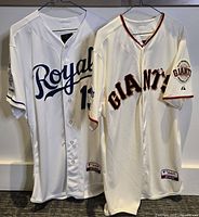 Two MLB jerseys hanging, one San Francisco Giants and one Kansas City Royals, both white with team logos and numbers visible.