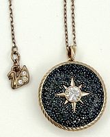 Close-up of the round Swarovski Collana locket pendant showing blue crystals with a central clear crystal in starburst design and the swan logo charm with crystals on the gold-tone chain.