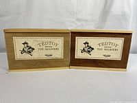 Two wooden boxes labeled Tedtoy American Toy Soldiers from the Camp Life Series, one light wood, one darker wood, boxed sets.