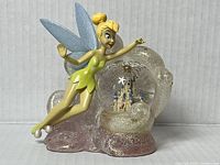 Front side view of Tinker Bell snow globe showing Tinker Bell flying and glitter globe with castle inside on pink glitter base.