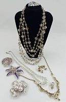 Display of all vintage costume jewellery items including multiple necklaces, several pins and brooches, and pairs of clip-on earrings arranged on a black mannequin bust and white background
