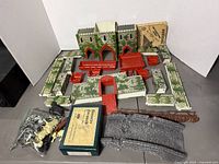 Complete collection of disassembled metal castle wall and tower parts, plastic figures in bag, boxed labeled pieces, and plastic bridge components on table.