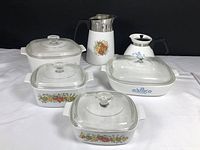 Overall lot of vintage Pyrex casseroles and coffee pots shown together on white background with black backdrop.
