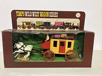 Photo of the stage coach toy in original branded box, showing the yellow and red coach with white horses and driver figure inside clear window.