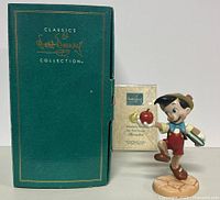 Full view of figurine with apple and book, along with original box and certificate of authenticity behind