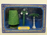 Front of box showing 3 accessories: green sculpted tree, green Main Street USA lamp post with white globes, silver Tomorrowland palm tree with green leaves.