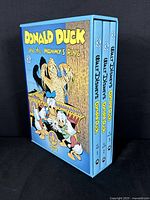 Slipcase showing all three volumes in blue with illustrated cover art of Donald Duck and nephews with mummy figure.