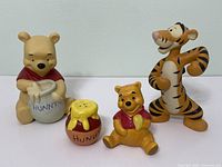 Four Winnie the Pooh themed items including two Pooh figurines, Tigger figurine, and two honey pot salt & pepper shakers, shown together on white background.