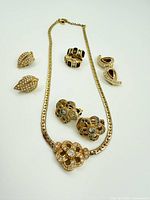 Full lot showing gold tone choker necklace and three pairs of clip-on earrings arranged on white background