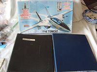 Photo showing the Monogram F-14 Tomcat model kit box alongside two binders containing aircraft manuals, one labeled Navion, the other plain blue.
