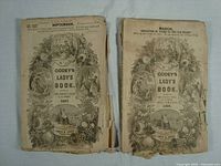 Front covers of two antique Godey's Lady's Book magazines dated 1864 and 1867 showing wear, tears, and detailed illustrated borders.