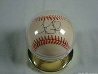 Top view of the autographed baseball in a protective clear plastic display case, showing the unknown autograph in black ink.