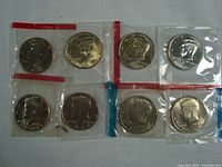 Top view of eight Kennedy half dollars in original mint cello packaging, arranged in two rows, showing obverse sides with profile of John F. Kennedy.