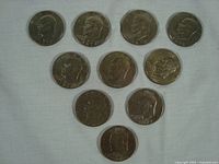 All ten Eisenhower silver dollar coins laid out on a fabric surface, showing front profile sides with visible years and details.