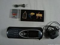 Photo showing Harley-Davidson Zippo lighter, Star Trek cloisonné pins on black backing, small metal toy bomb, Harmony remote control and charger.
