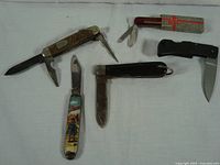 Wide shot of six assorted vintage pocket knives on white background showing variety of handles and blades.