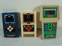 Photo showing all three handheld vintage electronic games side by side: blue Mattel Hockey, white Mattel Basketball, and beige Coleco Electronic Quarterback.