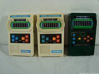 Photo showing all three handheld electronic football game consoles, two Football I units in cream color and one Classic Football 2 unit in dark green color placed side by side.