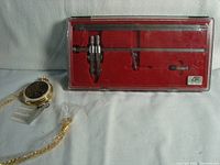 Lot showing drafting compass in clear case with red velvet interior and Franklin Mint pocket watch with gold-tone ornate casing and chain with tags