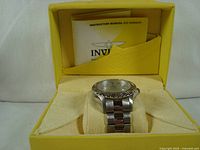 Invicta automatic wristwatch displayed in its original yellow box with instruction manual visible inside box compartment.