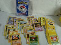Photo showing multiple stacks of vintage Pokémon trading cards with yellow borders and a visible card box in the back.