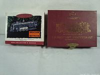 Photo showing the two original boxes of the Hallmark Lionel steam engine ornaments, including the Lionel 100th anniversary box in maroon with gold lettering and another box depicting a black steam engine illustration.
