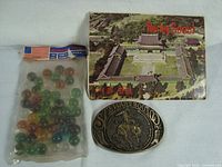 Front view of Stuart Boot Company brass belt buckle, sealed bag of Aqua Jewels marbles, and 1950s Seoul Korea postcards