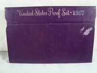 Purple cardboard outer envelope with silver text reading 'United States Proof Set 1987' showing shelf wear and some damage.