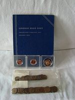 Photo of the Whitman Lincoln Head Cent Folder closed with two sealed packets of wheat pennies and three coin planchets in plastic holders placed on top of the folder.