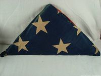 Folded 48 star flag showing blue field with white stars, displaying age wear and slight discoloration.
