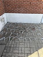 Six white cord outdoor icicle light strings laid out on a paved ground against brick and white wall background.