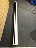 Photo of the entire rolled-up motorized projector screen lying on the floor showing its full length and white casing.