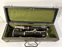 Clarinet disassembled in its green felt-lined case showing wooden body and metal keys.