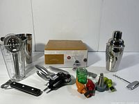 Full view of 4 martini glasses in box, cocktail shaker, bottle/can openers, drink plugs, and corkscrew on a white background