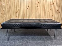 Side view of the black faux leather ottoman showing tufted cushion and metal leg structure.