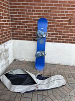 Snowboard standing against a wall with strap-in bindings and the protective bag laid out in front.
