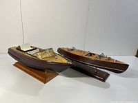 Photo showing both boats side by side on their wooden display stands highlighting the varnished wood and cream seating.