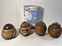 Photo showing four wooden tiki holders with carved faces and lids that act as piggy banks or cup holders positioned in a row
