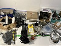 Wide view of the complete plumbing accessories kit laid out including the water pump, hoses, metal pipes, gauges, black plastic fittings and connectors, brass valve, zip ties, and boxed smaller parts.