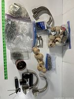 Full view of curtain rod accessory components laid on a white surface including wooden holders, metal hooks, suspension rods, assorted hardware in plastic bags, and decorative rings.