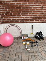 Wide view of exercise ball, hula hoops, spring trainer, racquet, and rollerblades against brick and white walls.