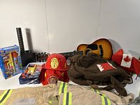 Wide shot of fireman costume pieces, hats, acoustic guitar, toy robotic grabber, and Canadian-themed clothing items.