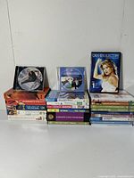 Photo of stacked fitness DVDs and VHS tapes, showing a variety of titles and genres including aerobic striptease, tai chi, yoga, pilates, and aerobics.