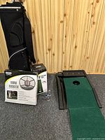 Full view of golf bag, Mini Mouth chipping net box, Izzo putting mat box, and Callaway putting return with green surface