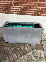 Exterior front angle view of the large rectangular gray planter showing smooth surface and size relative to brick background.