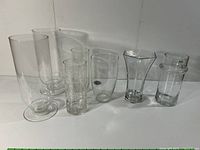 Front view of six clear glass vases with varied shapes and etched or textured designs arranged in a row against white background.