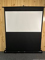 Front view of the projection screen set up, showing a white viewing area with black borders in a wooden paneled room.