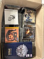Box of mixed music CD jewel cases, showing a variety of album covers visible on top and edges, indicating an eclectic music collection.