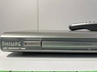 Front view of Philips DVD player showing PHILIPS logo, power button, and DVD tray with remote placed on top.