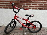 Full side view of red kids bicycle showing frame, wheels, pedals, and kickstand.